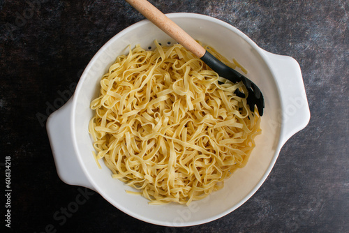 Cooked Tagliatelle Pasta in a Large Colander with a Pasta Spoon: Freshly cooked and drained noodles in a large strainer with a pasta fork