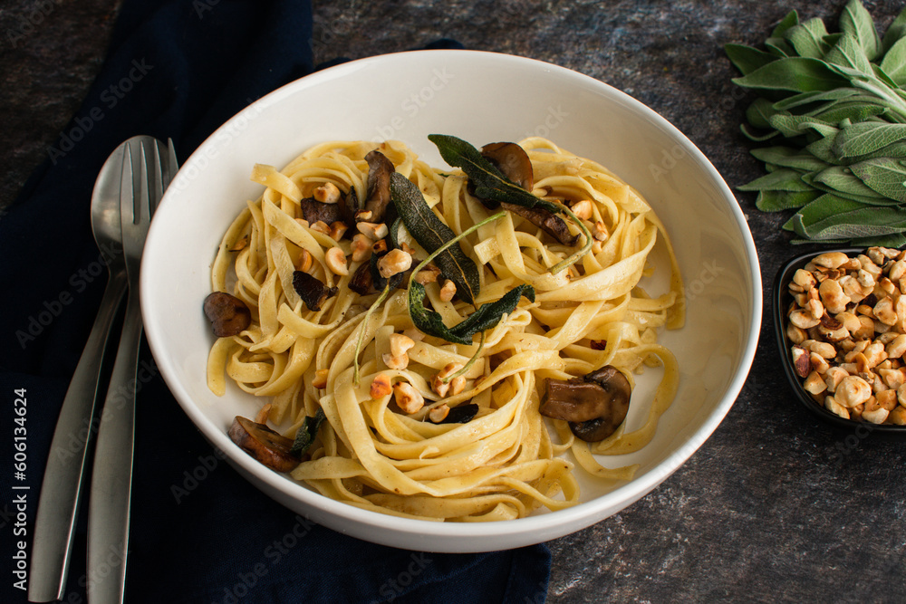 Tagliatelle with Mushrooms, Sage Butter, and Toasted Hazelnuts in a Pasta Bowl: A serving of noodles topped with fried sage leaves in a shallow bowl