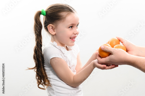 A little girl is given tangerines on a white background, the child takes tangerines.