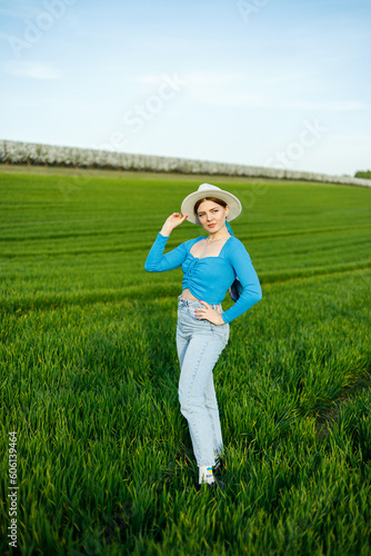 Young attractive woman in white hat, blue shirt, blue jeans, posing in summer green field. Copy, empty space for text