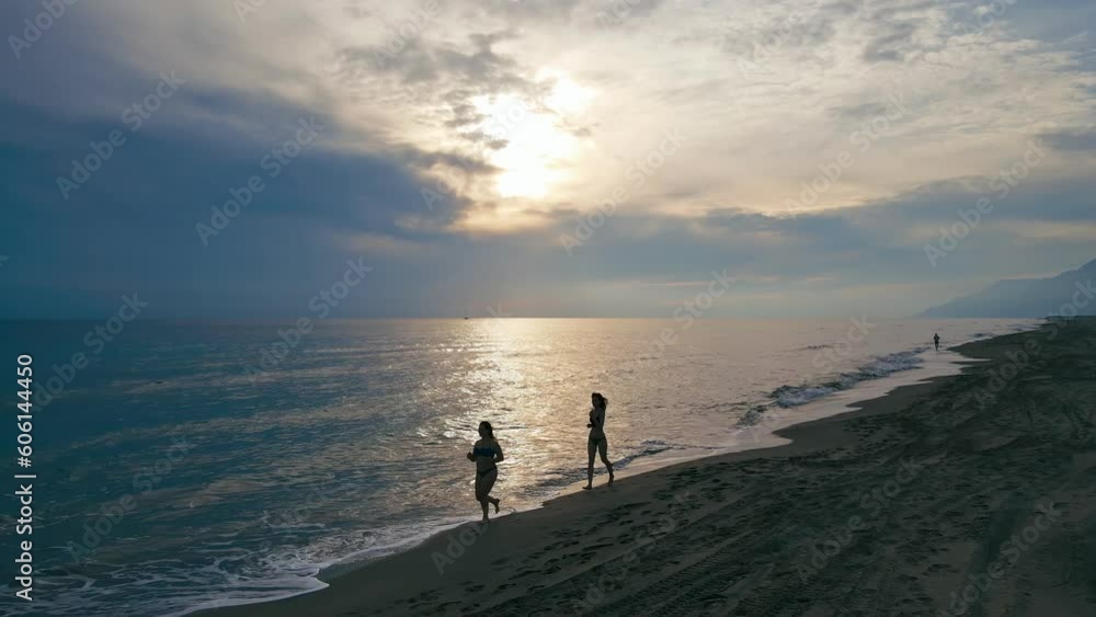 Two attractive young women in bikini jogging on beach in sunset time