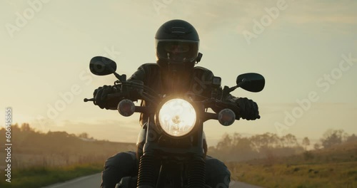 Man biker driving a black chopper motorcycle during a sunset.