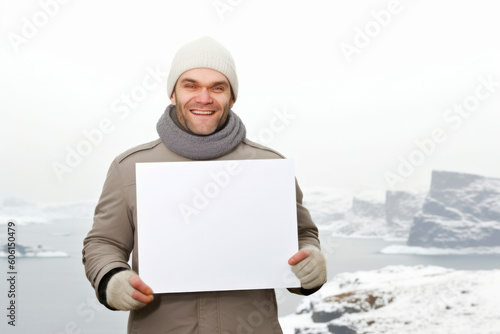 Young man holding a blank sheet of paper in front of a frozen lake