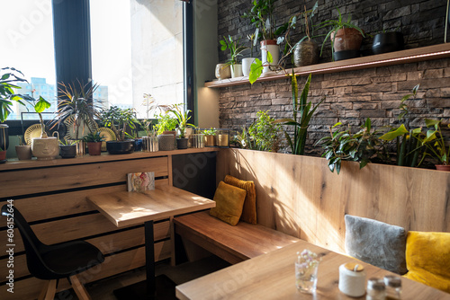 Interior of modern vegan restaurant with many plants as decoration with wooden tables and stone wall.