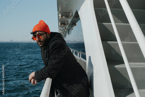 an image of a young man from the Middle East, standing on a ferry and enjoying the serenity of the environment