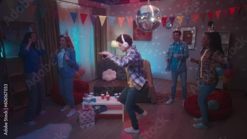 A guy in white headphonesturns on the music on his phone and begins to dance vigorously. His friends look at him in shock, surprise, and dance to different music in the room.