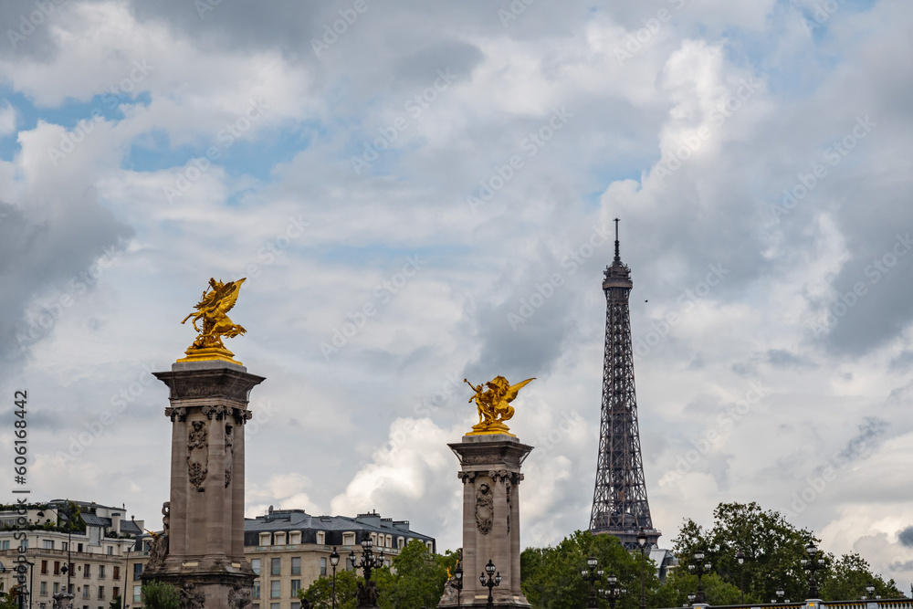 Fototapeta premium Renowned gilt bronze surmounted pylon of the Alexandre III bridge with the Eiffel tower in background from the Seine, in Paris, France