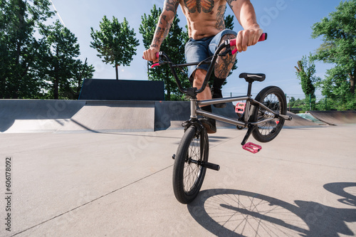 Cropped picture of a tattooed middle-aged unrecognizable man doing stunts and freestyle tricks on a bmx in a skate park.