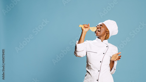Young happy chef using wooden spoon to sing in studio, having fun singing with cooking utensils on camera. Professional cook with apron playing aroung and holding kitchen tool. photo