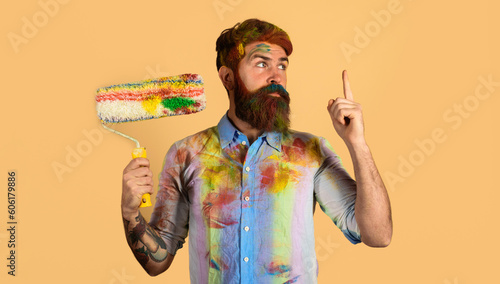 Painter man with paint roller pointing finger up. Professional painter, decorator, builder worker with paintroller. Handsome bearded worker, repairman or handyman in dirty dye shirt with paint roller. photo