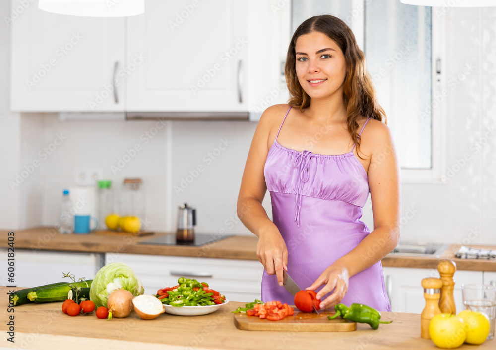 Smiling young housewife in purple nightgown cooking dinner in the kitchen at home