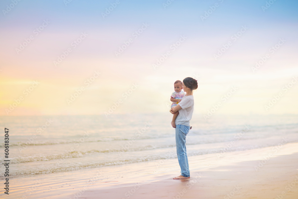 Mother and baby on tropical beach at sunset.
