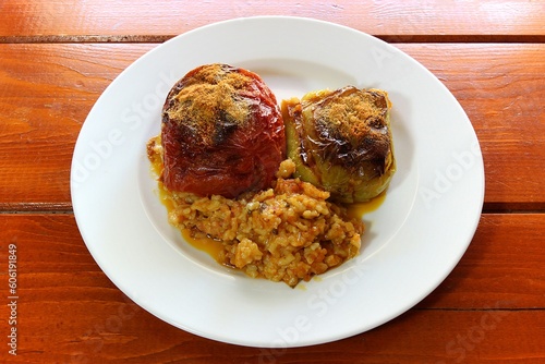 Stuffed tomatoes and peppers, a classic Greek dish, are displayed on a white plate against a background of a wooden table. Selective Focus photo