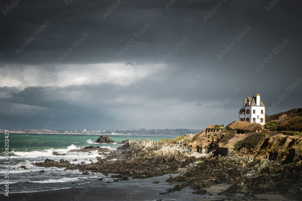 Isolated white house on the rocky coast of Brittany in France in a bad weather sky