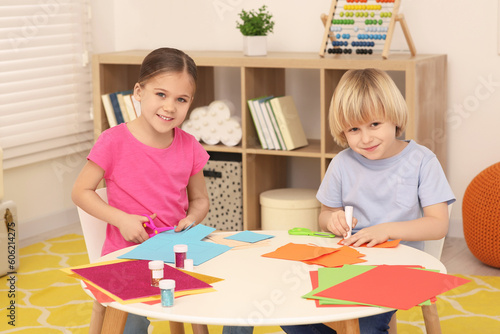 Girl cutting colorful paper and boy using glue stick at desk in room. Home workplace