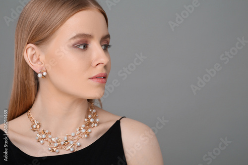 Beautiful young woman with elegant jewelry on gray background, space for text
