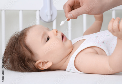 Father cleaning nose of his baby with cotton bud on bed, closeup
