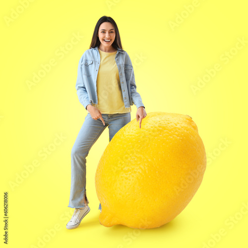 Happy young woman with big lemon on yellow background