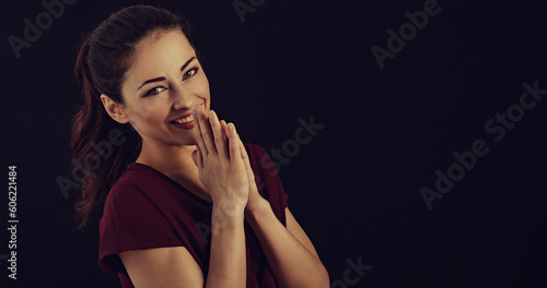 Beautiful excited laughing thinking business woman holding hands near the face have an idea in dark red t-shirt on black background with empty copy space for text. Closeup toned