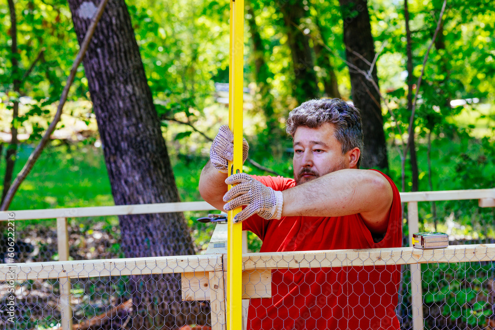 Obraz premium Levelling new wooden domestic chicken coop built on farm with metal mesh inside using level worker