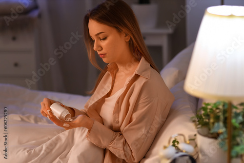 Young woman taking pills before sleep in bedroom photo