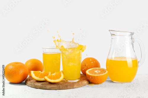 Jug and glasses of fresh orange juice with splashes on white background