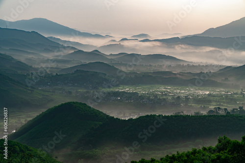 Hilly telephoto landscape with green forest, covered with mists in the early morning. Along with valleys and fields.