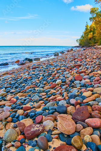 Distant green trees with partly cloudy blue sky sapphire waters and a shore of colorful stones photo