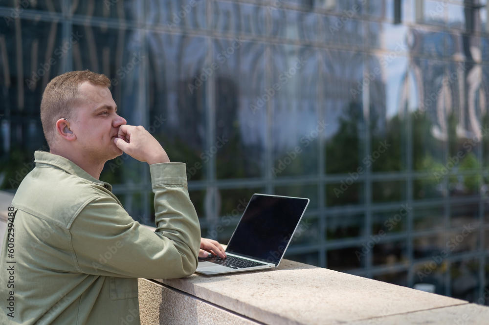 Sad guy with hearing aid using laptop outdoors. Sad guy with hearing aid using laptop outdoors.