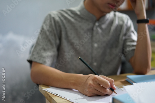 Man writing on a notebook while studying, working, or take exam