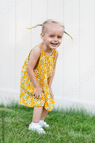 Little beautiful girl posing in summer dress on green grass and white background