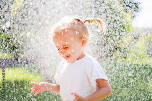 A beautiful girl in a dress plays on a green lawn and splashes with water