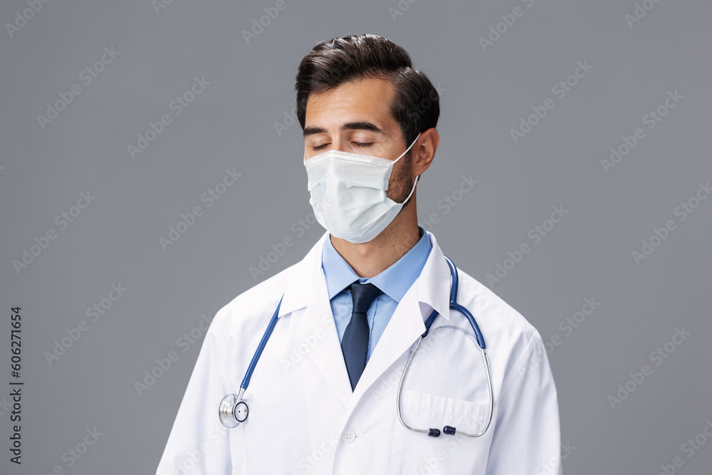 A male doctor in a white coat and medical mask and sterile gloves looks at the camera on a gray isolated background, copy space, space for text A male doctor in a white coat and medical mask and sterile gloves looks at the camera on a gray isolated background, copy space, space for text