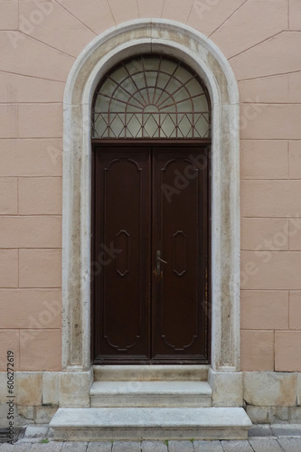 street view of old wooden door with arched frame against pink wall in Croatia