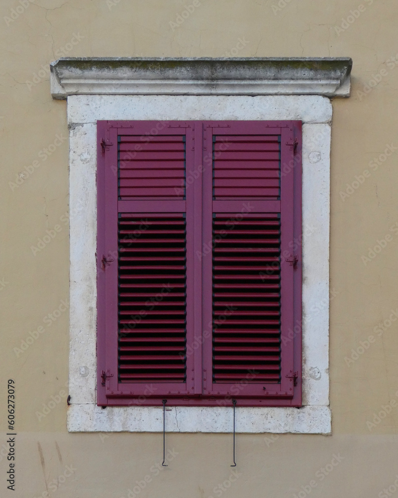 window with red shutters against white stone frame on cream color building exterior in Croatia