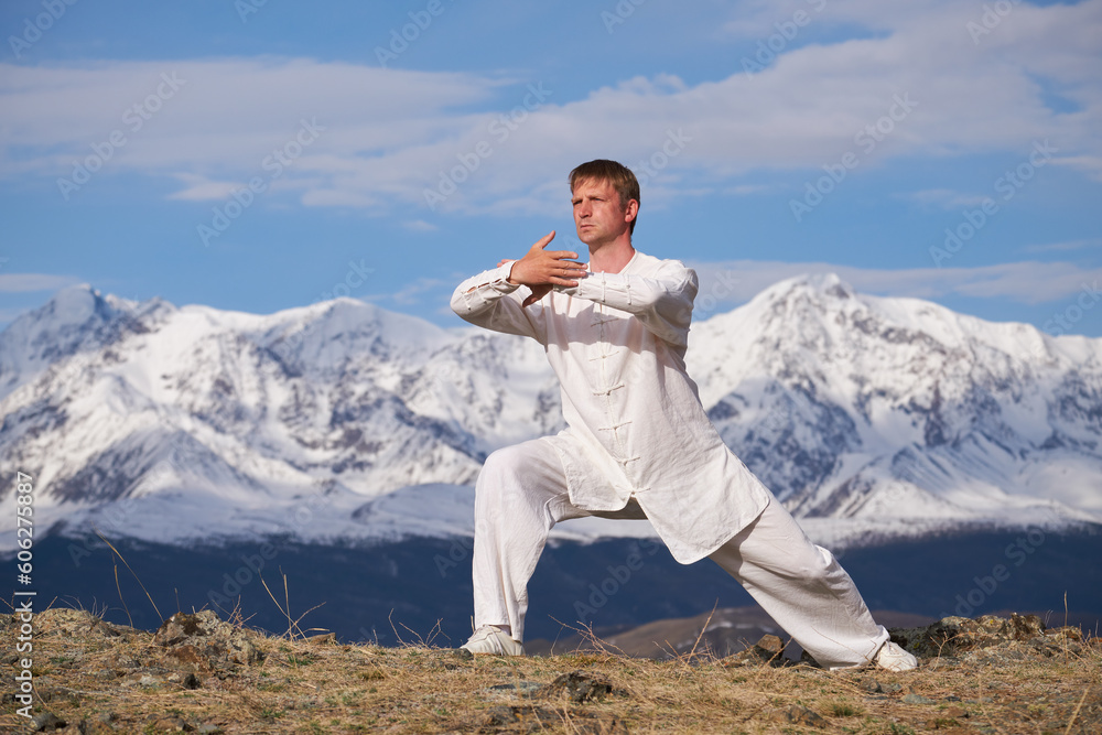 Wushu master in a white sports uniform training kungfu in nature on background of snowy mountains.