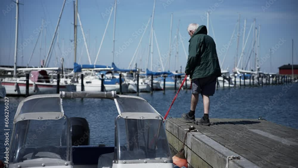 Elderly man attaching small boat to the pier on a harbor in Sweden, blue sky Elderly man attaching small boat to the pier on a harbor in Sweden, blue sky