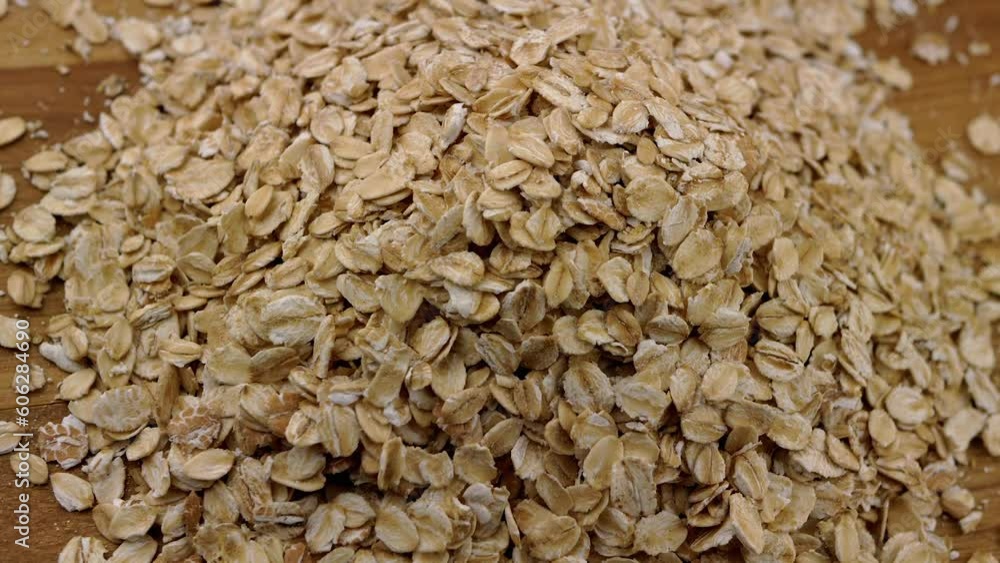 Close up, Pile Dry Oat Flakes Slowly Rotate on a Wooden Plate or Cutting Board. Top view. Texture grain. Turn, rotating. Hill of scattered raw oatmeal. Healthy diet breakfast. Useful food. Fast food. Close up, Pile Dry Oat Flakes Slowly Rotate on a Wooden Plate or Cutting Board. Top view. Texture grain. Turn, rotating. Hill of scattered raw oatmeal. Healthy diet breakfast. Useful food. Fast food.
