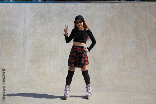 Aggressive inline roller blader female posing in a concrete skate pool. Friendly young person standing in a skatepark and showing peace sign