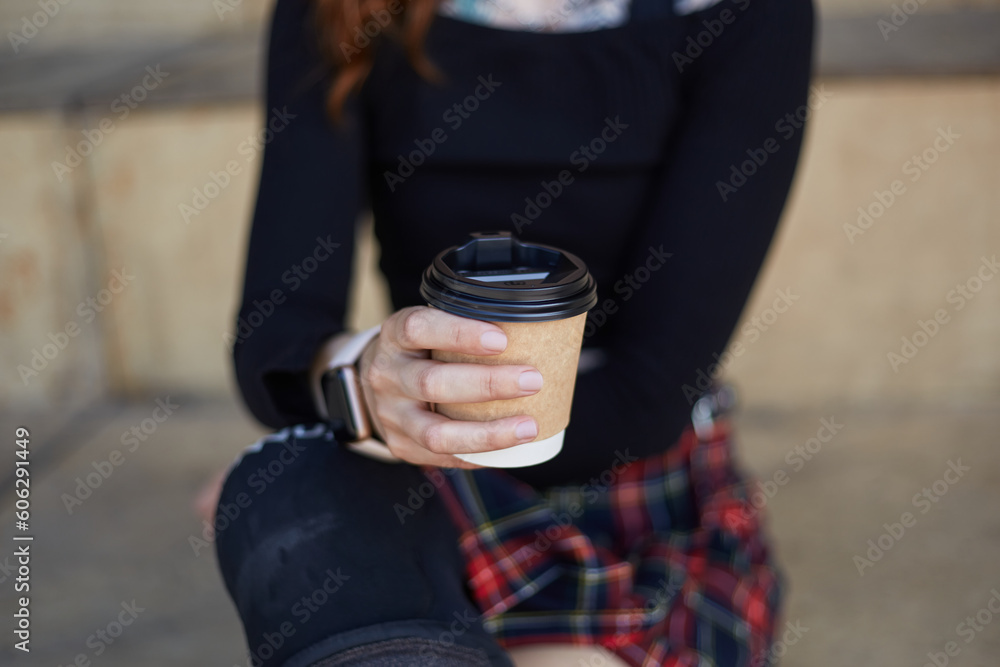Unrecognizable skater girl wearing modern smart wrist watches and sitting in a skatepark with a cup of coffee in hand Unrecognizable skater girl wearing modern smart wrist watches and sitting in a skatepark with a cup of coffee in hand