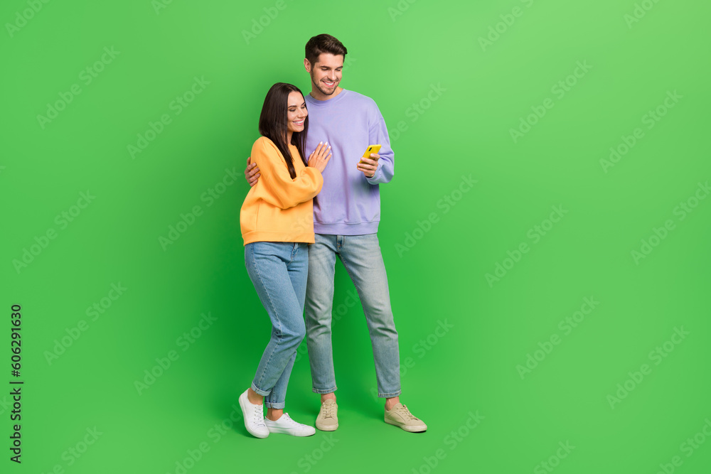 Full body photo of two positive partners cuddle use telephone empty space isolated on green color background Full body photo of two positive partners cuddle use telephone empty space isolated on green color background