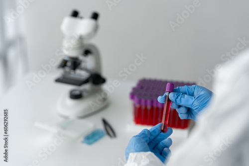 A scientist or medical technician wearing PPE and wearing a glove holds patient-derived blood vessels and researches them in a sample rack to prepare for testing and qualitative concentrations.