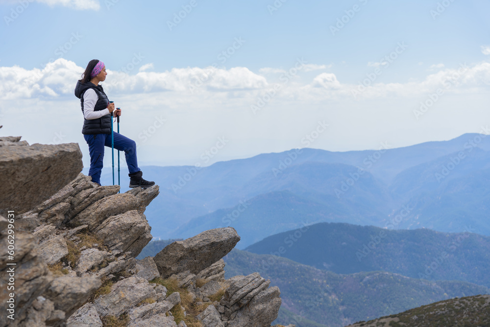Latin woman leans on a rock with her sticks and looks ahead contemplating a splendid landscape after a hard and long day of hiking and trekking