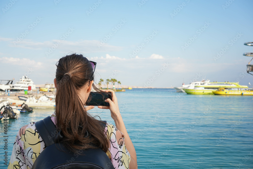 Young beautiful girl taking a picture of yachts at a docking bay in the sunset Young beautiful girl taking a picture of yachts at a docking bay in the sunset