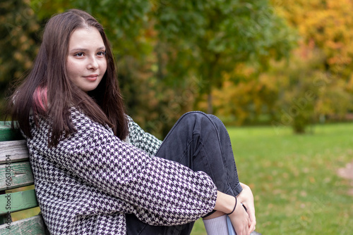 Close-up of a young woman sitting on a bench in an autumn park.