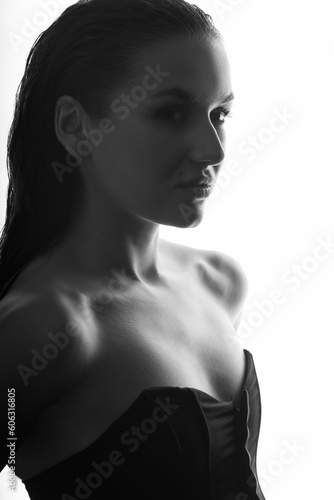 Portrait of beautiful and sexy woman silhouette with black corset and wet hair in glowing studio background. Model standing in grace pose and looking aside camera. Black and white image