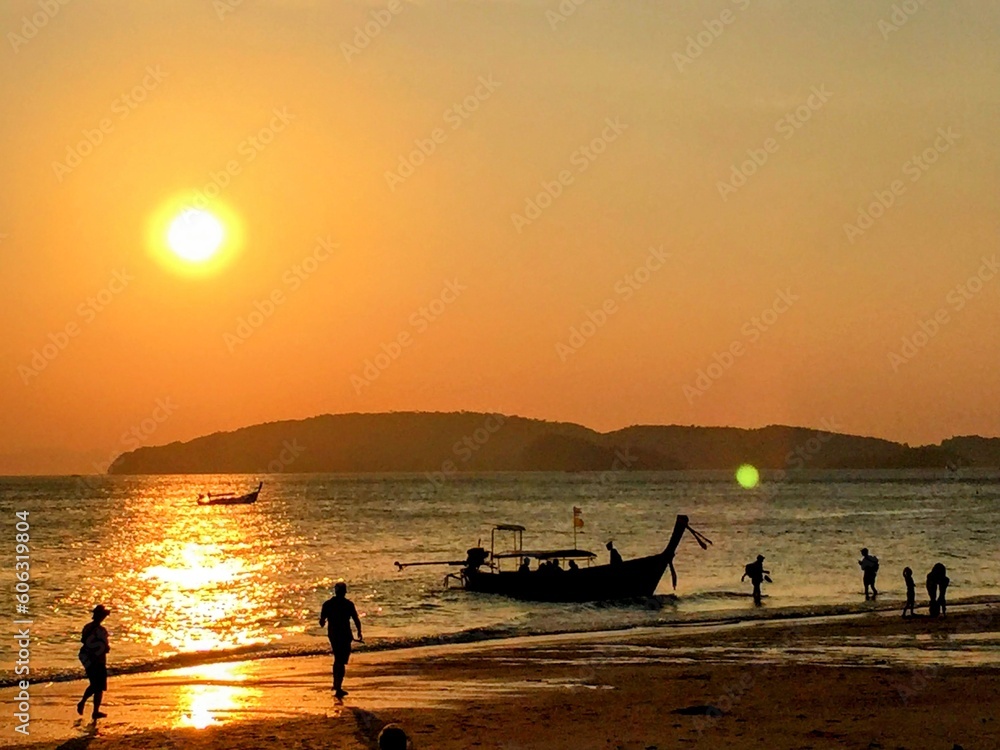 Beautiful tranquil sunset over the sea with fishermen long tail boat and few people dark silhouettes on the beach