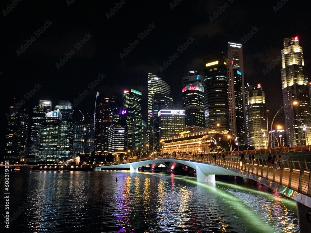 Urban cityscape night view with neon lighted skyscrapers, bridge and reflection in the river water channel 