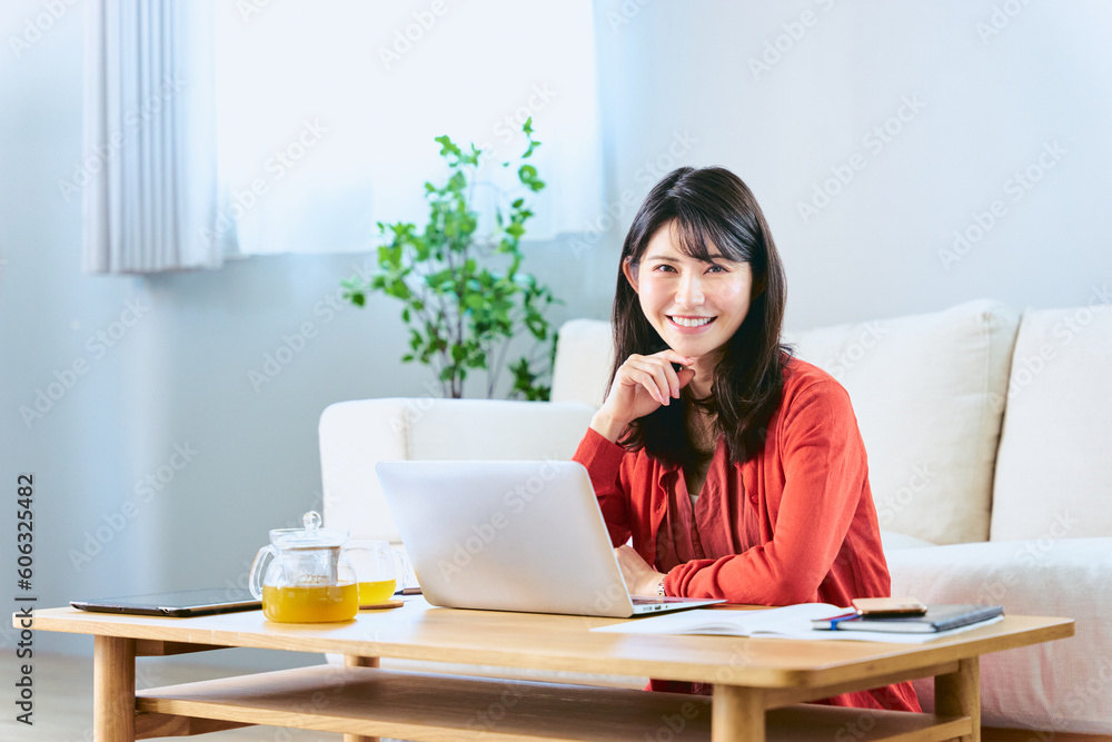 リビングのローテーブルのノートパソコンでテレワークをして働く1人の30代の女性の笑顔のカメラ目線 リビングのローテーブルのノートパソコンでテレワークをして働く1人の30代の女性の笑顔のカメラ目線