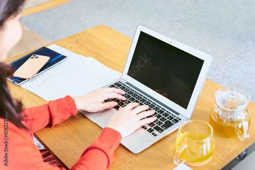 リビングのローテーブルにパソコンを広げキーボードでタイピングをして入力作業をする30代女性の手元 photo